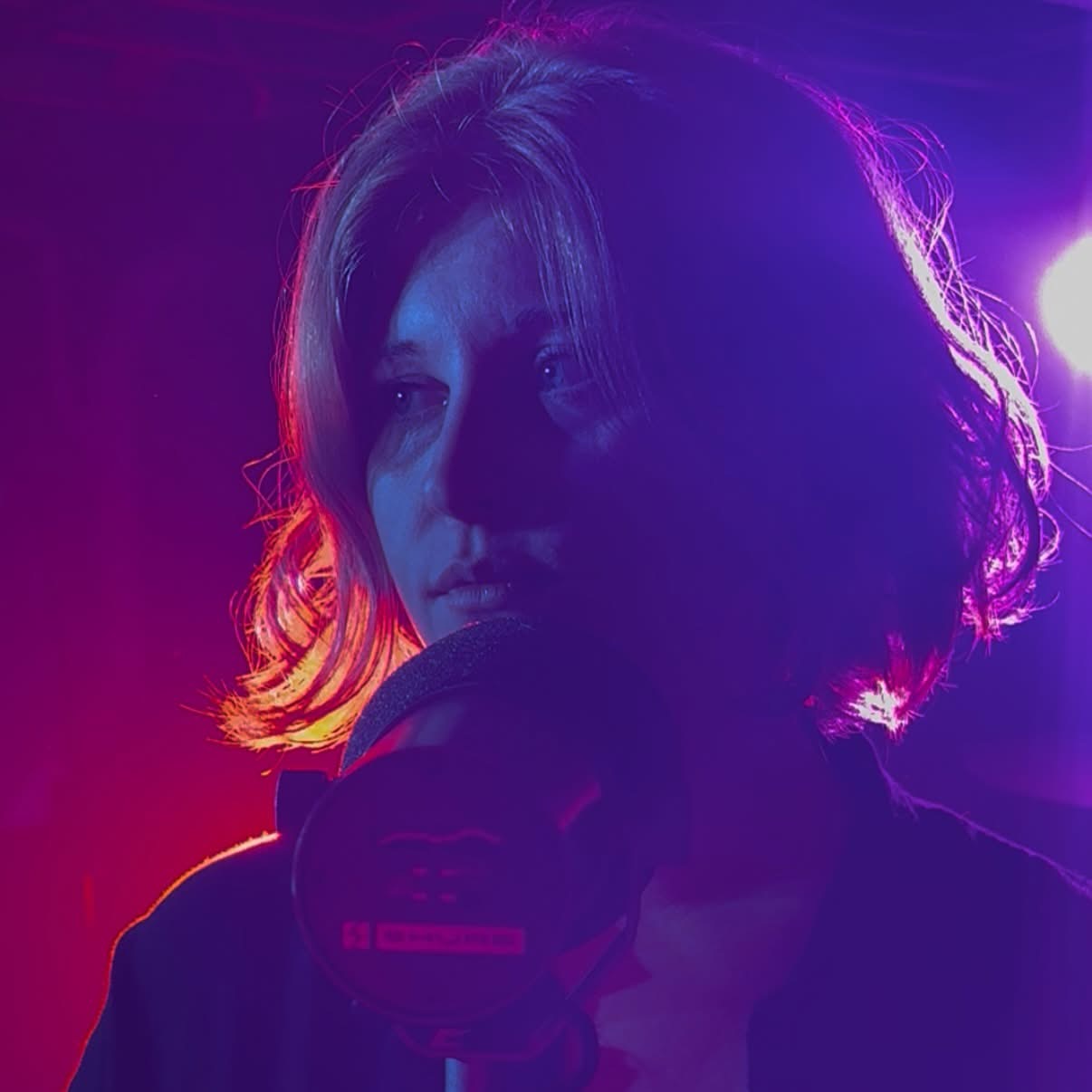 Maggie Moon holding a microphone under neon blue and purple stage lighting